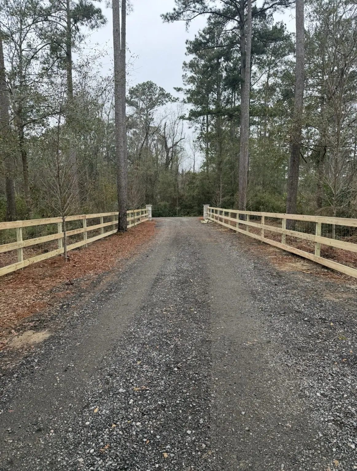 Wood and wire farm fencing on both sides of a gravel driveway