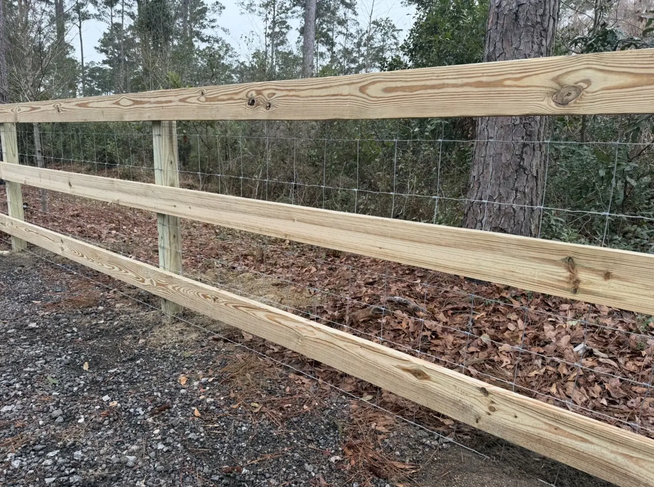 Three-rail pressure-treated wood fence with wire mesh