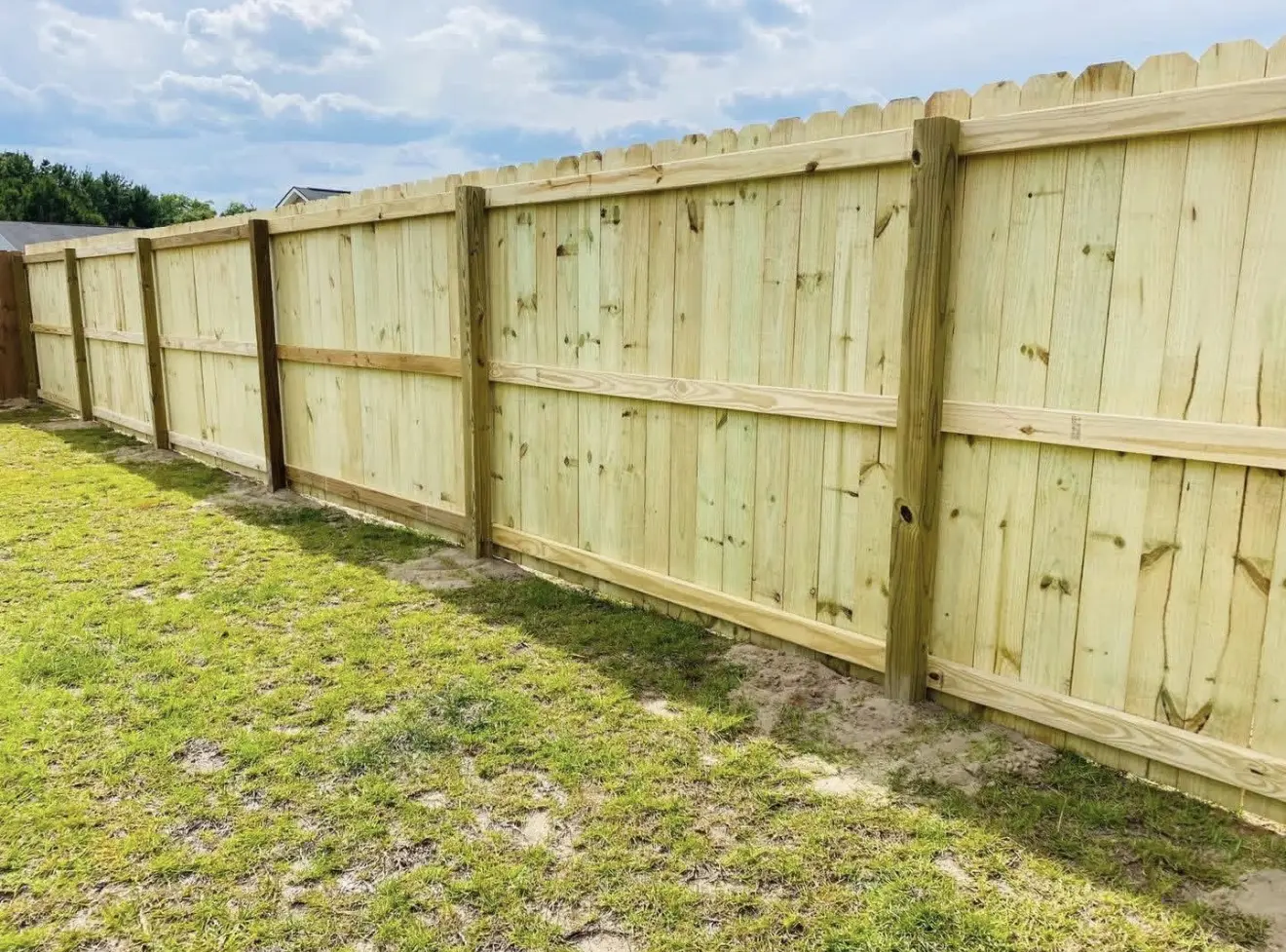 Inside view of a long pressure-treated stockade privacy fence across a residential lawn
