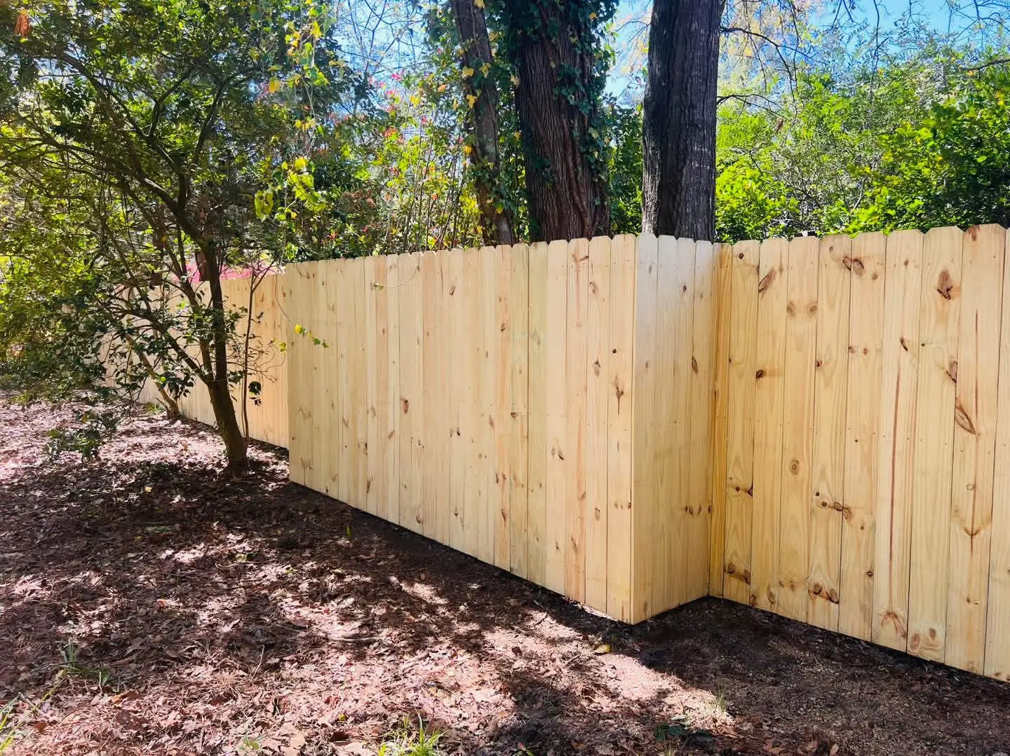 Solid pressure-treated stockade privacy fence wrapping around a wooded residential yard